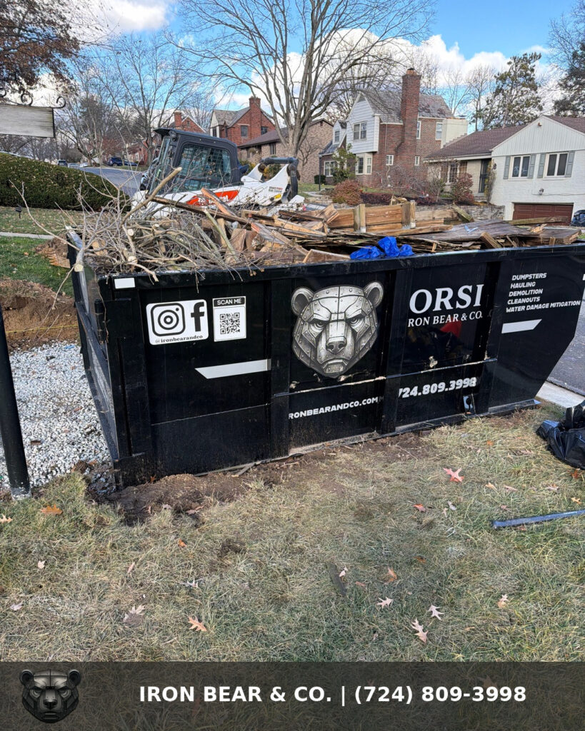 Iron Bear & Co. dumpster in a residential front yard loaded with broken-down lumber and brush from an outdoor teardown