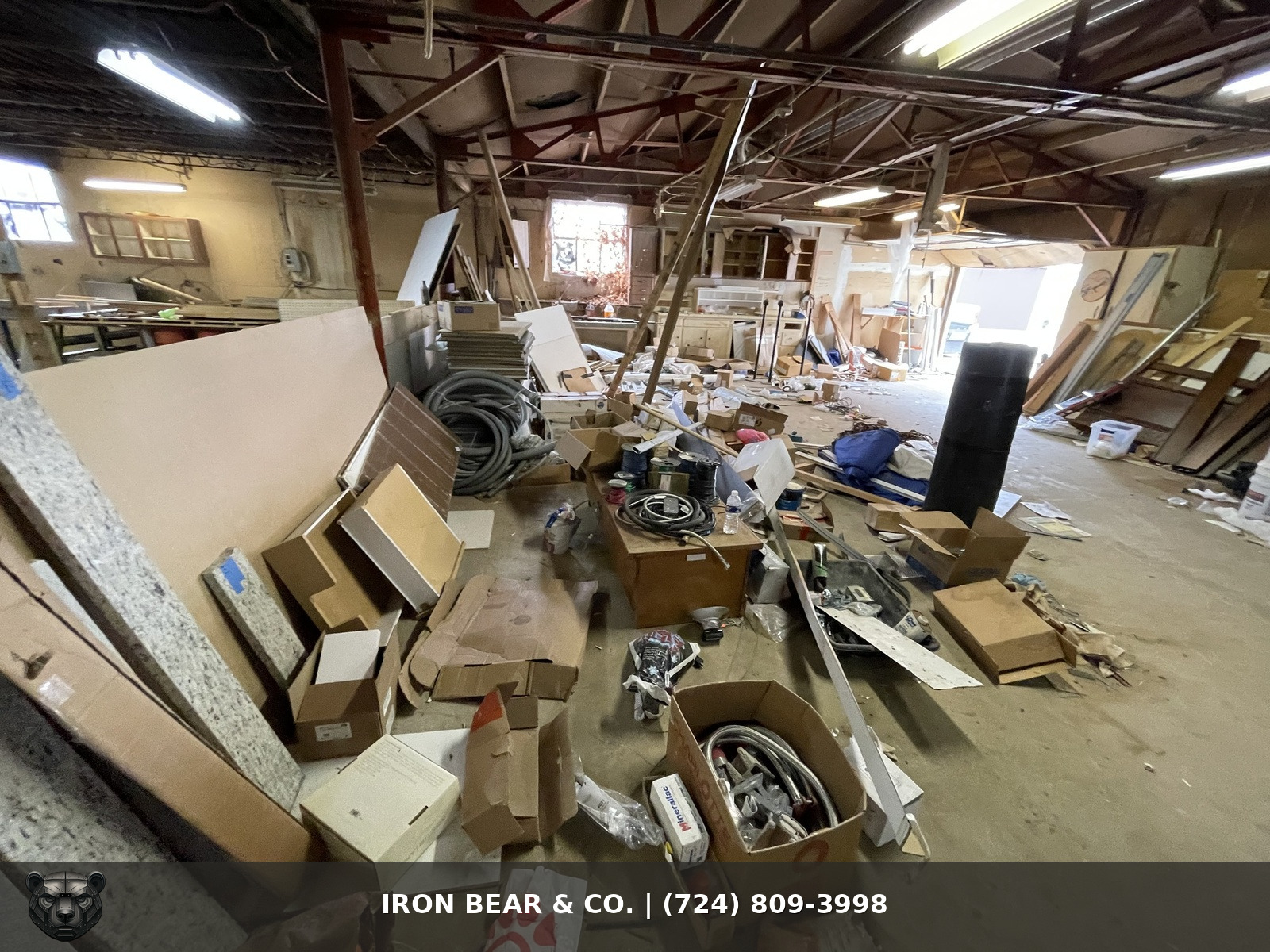 Commercial warehouse floor covered with old cabinets, boxes, cables, and leftover materials before an Iron Bear & Co. cleanout